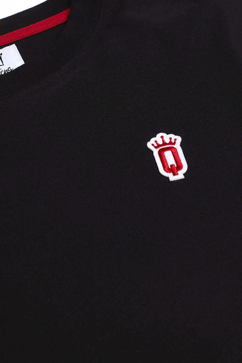 Close-up of embroidered red Q with crown patch on black cotton fabric of QCC T-shirt